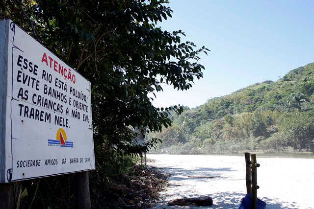 Sign reads 'This river is polluted. Avoid swimming and keep children away.'